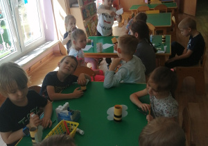 Dzieci przy stolikach przyklejają elementy papierowe do rolki i wykonują pszczółkę